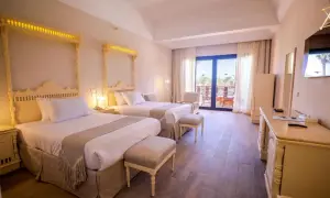 Pokój hotelowy z dwoma łóżkami, ozdobnymi zagłówkami i wyjściem na balkon. Idealne miejsce na wakacyjny calimera.