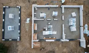 Budowa domu z bloczków betonowych. Materiały budowlane leżą na płycie fundamentowej, czekając na montaż ścian, by zapewnić niski współczynnik przenikania ciepła.