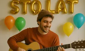 Uśmiechnięty mężczyzna gra na gitarze, a za nim złote balony tworzą napis "STO LAT". Dowiedz się, jak zagrać sto lat na gitarze.