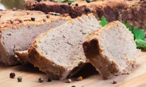 Pokrojony pasztet mieszany drobiowo-wieprzowy, przyprawiony ziarnami pieprzu, na desce.