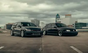 Dwa czarne Volkswageny: sportowy hatchback GTI i sedan, zaparkowane na dachu parkingu z widokiem na miasto.