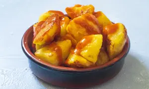 Knusprige Kartoffelstücke, überzogen mit einer würzigen Sauce, serviert als köstliche Patatas Bravas in einer rustikalen Schale.