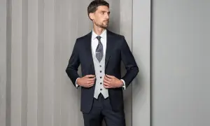 Elegancki mężczyzna w granatowym garniturze, jasnej kamizelce i wzorzystym krawacie. Idealny strój na wesele, czy mucha lepsza?