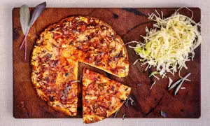 En hel och en skivad pizza på en träskärbräda, med en hög strimlad kål. En klassisk kombination som ger en hint om pizzasallad ursprung.