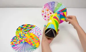 Manos creando un caleidoscopio con manualidades con material reciclado. Tubo de cartón decorado y discos circulares con patrones coloridos.