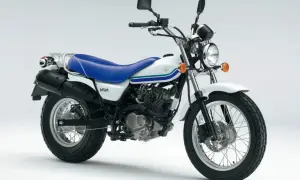 Biały motocykl Suzuki Van Van z niebieskim siedzeniem i zielono-niebieskimi pasami na baku. Idealny na miejskie wyprawy.
