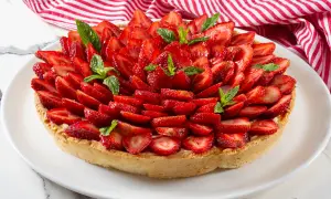 Deliziosa crostata alla crema, ricoperta da fragole fresche affettate e guarnita con foglie di menta.