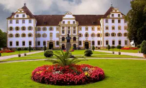Prachtvolles Schloss Salem mit symmetrischer Fassade, gelben Akzenten und einem gepflegten Garten voller Blumen und Bäume.