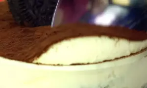 Une cuillère plonge dans un délicieux tiramisu Oreo, saupoudré de cacao. Un dessert gourmand à savourer !