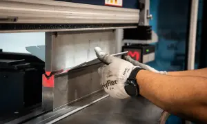 Operator w rękawicach formuje metal na prasie krawędziowej. Różne rodzaje prasy pozwalają na precyzyjne gięcie.