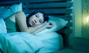 A woman lies awake in bed, her eyes wide open, a picture of paradoxical insomnia. The room is bathed in a cool, blue light, emphasizing her distress.