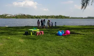 Dzieci bawią się nad jeziorem Mikorzyńskim. Na trawie kolorowe zabawki: piłki, stolik i krzesełka.
