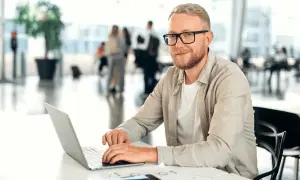 Mężczyzna w okularach, z brodą, pracuje na laptopie. Jego kod zawodu to informatyk, który tworzy cyfrowe rozwiązania.