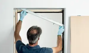 Installazione controtelaio porta scorrevole in cartongesso. L'operaio con guanti azzurri posiziona la guida superiore.