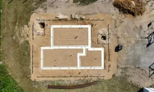 Widok z lotu ptaka na budowę domu. Widać gotowy fundament, piasek, wykopy i materiały budowlane.