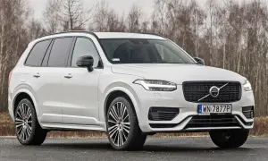 Białe Volvo XC90 T6 z czarnymi felgami stoi na drodze, za nim las.