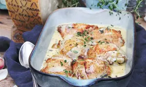 Kycklinglår i krämig sås, toppad med färska örter. En bit Grana Padano-ost syns i bakgrunden, redo att rivas över.