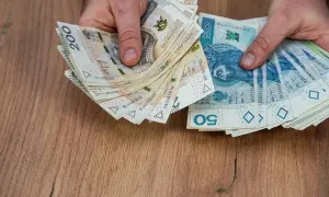 Dłonie trzymają stos banknotów 200 zł i 50 zł. Może to być wypłata pieniędzy przed śmiercią, jako testament.