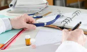 Lekarz pisze receptę, obok stetoskop i leki. Czy do dermatologa na NFZ trzeba mieć skierowanie?