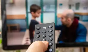 Dłoń trzymająca pilot do telewizora, na ekranie widać scenę z dzieckiem i mężczyzną. Czas na ulubiony serial, opłacony abonament radiowo-telewizyjny działa!