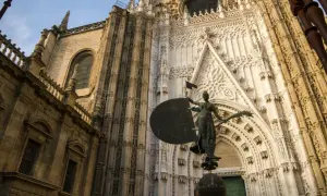 Estatua frente a la imponente fachada de la catedral de Sevilla, con detalles góticos y una escultura que evoca la navegación.