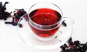 Szklana filiżanka z czerwonym naparem, obok suszone płatki hibiskusa. Idealny napój na odchudzanie.