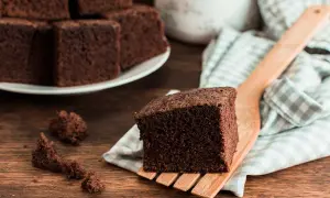 Un trozo de bizcocho de chocolate esponjoso servido en una espátula de madera, con más trozos apilados en un plato al fondo.