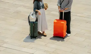 Para podróżnych z bagażami, w tym zielona podręczna walizka na kółkach Wizzair, gotowa na wakacje.