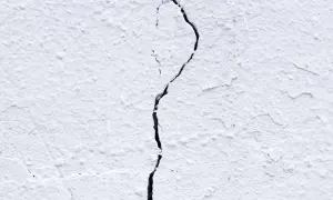 Una pared blanca con textura rugosa muestra grietas por dilatación, una línea oscura que se abre paso a través de la superficie.
