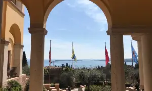 Arco con vista sul lago, giardini e bandiere che sventolano, ricordando l'atmosfera della villa d'Annunzio.