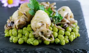 Delizioso piatto di seppie con piselli, guarnito con prezzemolo e erbe aromatiche, servito su una pietra scura.