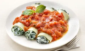 Cannelloni ricotta épinard généreusement nappés de sauce tomate, garni d'une feuille de basilic. Un plat savoureux et réconfortant.