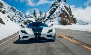 Biały Koenigsegg Agera z czarnym pasem pędzi po ośnieżonej górskiej drodze.