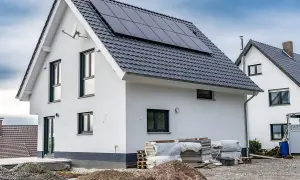 Nowy dom z panelami słonecznymi na dachu, w trakcie rozbudowy. Wokół materiały budowlane.