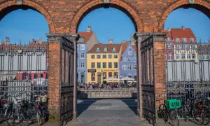 Kopenhaga nietypowe miejsca: kolorowe kamienice nad kanałem, widok przez zabytkową bramę z rowerami.