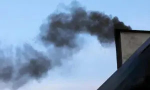 Gęsty, czarny dym wydobywa się z komina, tworząc kłęby na tle błękitnego nieba. Ten smród z komina w pokoju jest nie do zniesienia.