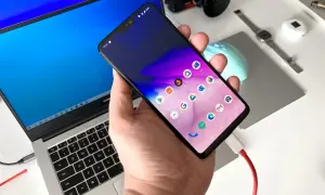 Dłoń trzyma smartfon podłączony kablem do laptopa, ułatwiając automatyczne przesyłanie zdjęć z telefonu na komputer.