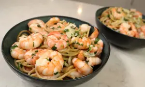 Pyszny makaron z krewetkami, posypany świeżą natką pietruszki i parmezanem, podany w ciemnych miseczkach.