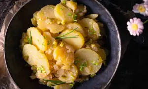 Schüssel mit Kartoffelsalat ohne Mayo, garniert mit Schnittlauch und Gurkenstückchen.