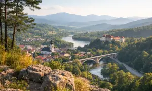 Widok na miasteczko z rzeką, mostem, kościołem i zamkiem na wzgórzu w otoczeniu gór.