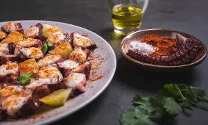 Un plat de poulpe à la gallega, garni de pommes de terre et d'épices, avec un petit bol de paprika et de sel, et un verre d'huile d'olive.