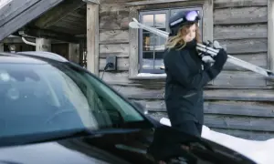 En person med skidor laddar bilen i minusgrader vid en timrad stuga.