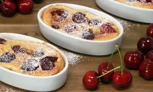 Deux clafoutis sans oeuf aux cerises, saupoudrés de sucre glace, sur une table en bois. Des cerises fraîches sont disposées autour.