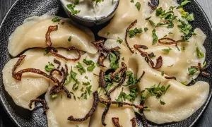 Pyszne pierogi z ziemniakami i boczkiem, posypane chrupiącą cebulką i natką pietruszki. Idealne z kwaśną śmietaną.