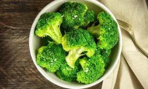 En skål med nykokt, grön broccoli, strödd med flingsalt. En gaffel ligger bredvid på en beige duk.
