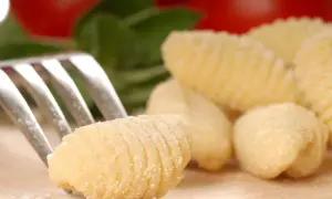 Une fourchette pique un gnocchi fait maison, prêt pour une délicieuse recette gnocchi. Des gnocchis frais et des ingrédients italiens en arrière-plan.
