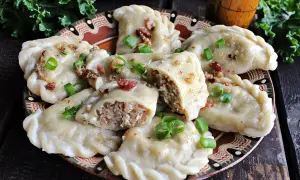 Pyszne pierogi z kaszą gryczaną i serem białym, okraszone skwarkami i szczypiorkiem, na ozdobnym talerzu.