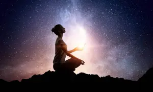 Silueta de mujer meditando bajo un cielo estrellado, sosteniendo una luz brillante. Conexión cuantica espiritual.