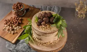 Kuchen ohne backen, verziert mit Schokoladentrüffeln, gehackten Haselnüssen und grünen Blättern. Daneben ein Glas mit Haselnüssen.
