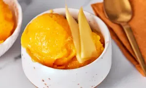 Erfrischendes Mango Sorbet in einer Schale, garniert mit Mangostücken. Daneben ein Löffel auf einem orangen Tuch.